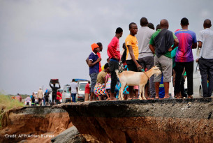 Locals stand beside a damaged section of the road with a goat after Cyclone Idai