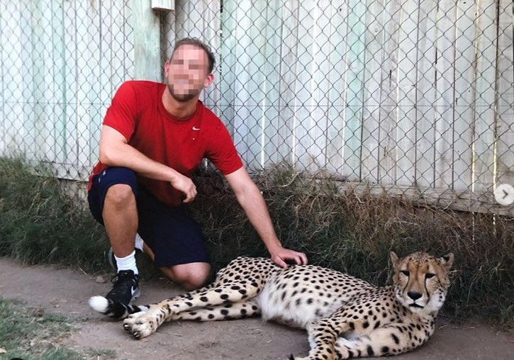 A man posing with a captive cheetah for a photo